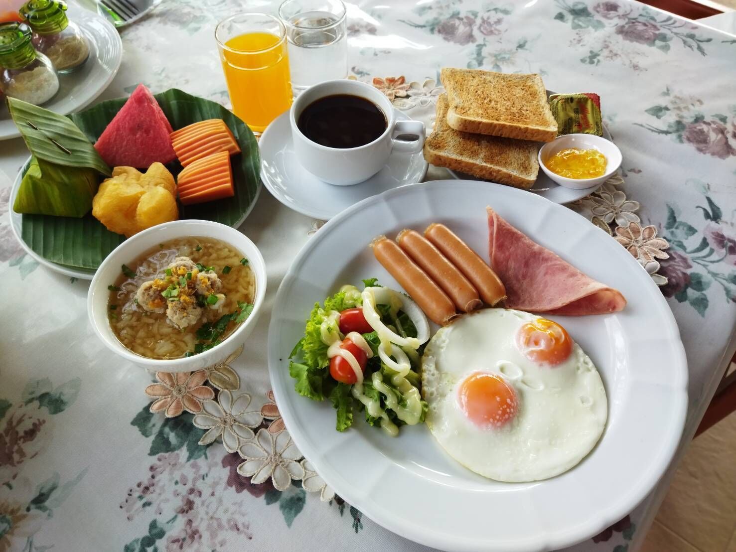 Un plato de desayuno con huevos, salchichas, jamón y un tazón de sopa.