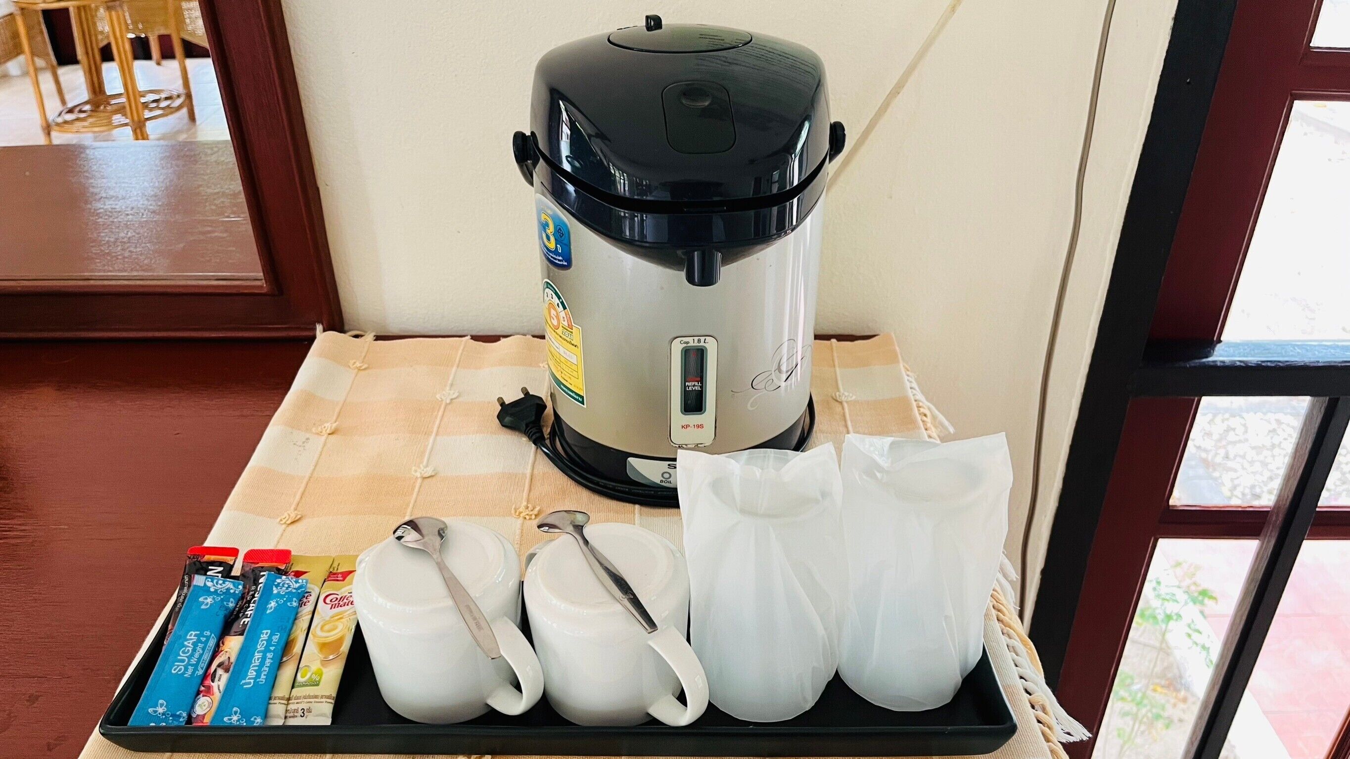 A coffee maker on a table with sugar packets, a white mug, and a white bag.
