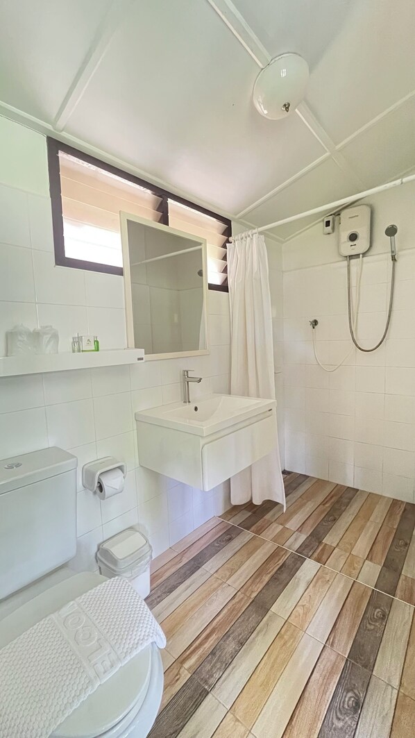A bathroom with a wooden floor, white tiles, a sink, a toilet, and a shower. - Suan Bankrut Beach Resort (Bang Saphan)