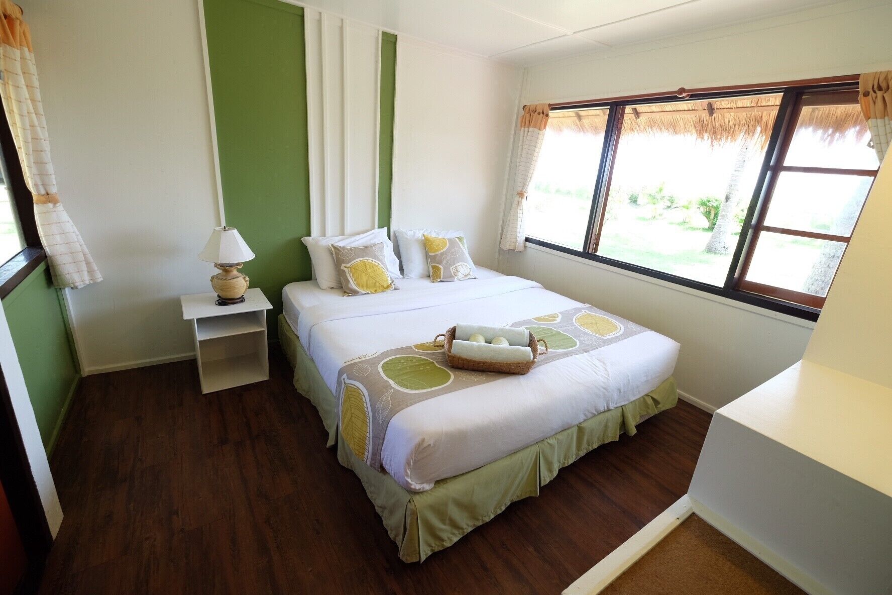 A neatly arranged bedroom with a bed, bedside table, lamp, and a window with a view of greenery.