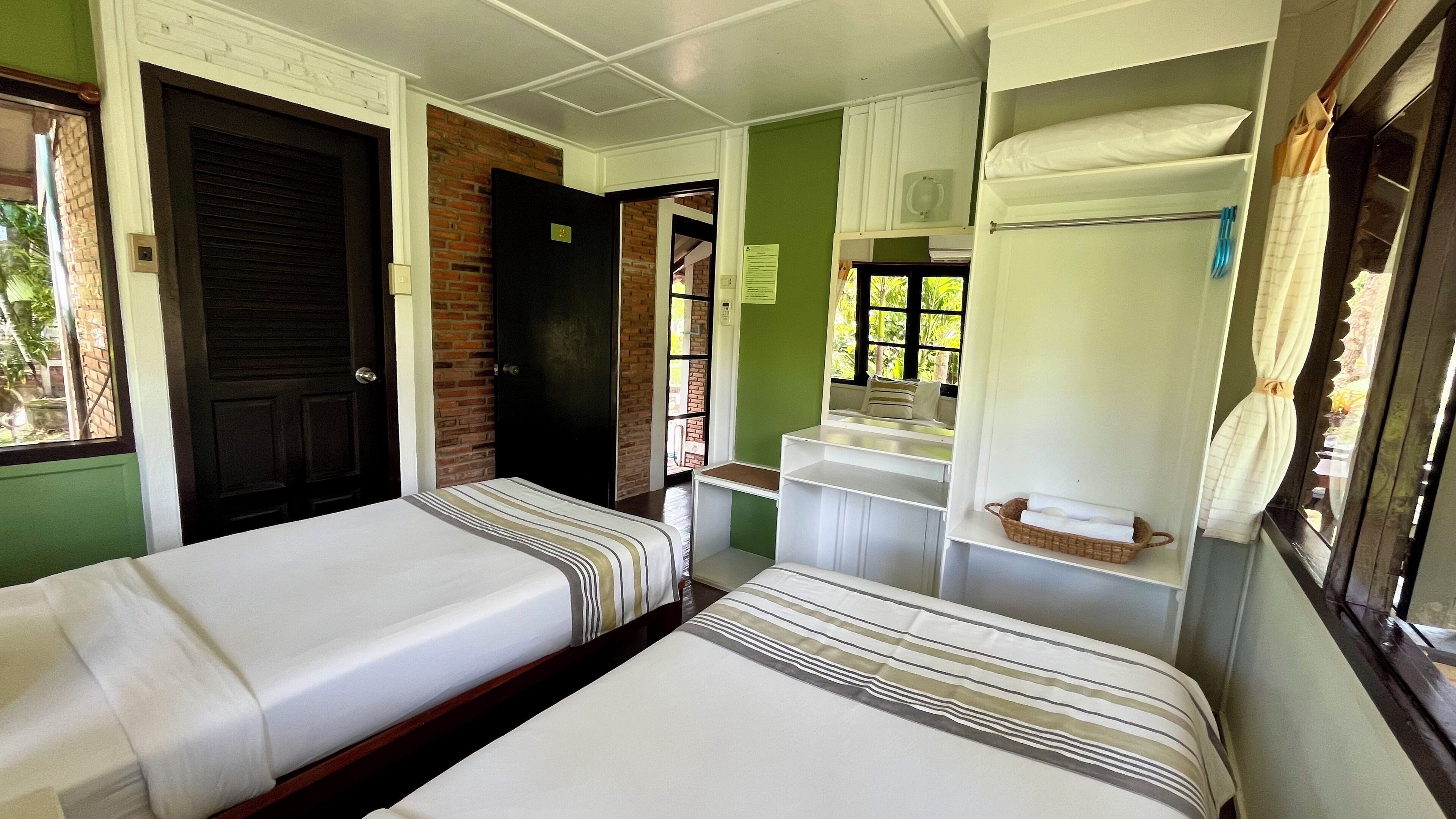 Una habitación con dos camas individuales, un pequeño rincón de cocina, un ventanal con vistas y una puerta que da a otra habitación.