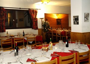 A dining area with round tables set for a meal, featuring wine glasses, bottles, and red napkins. - Hotel L'Aigle (Valmeinier)