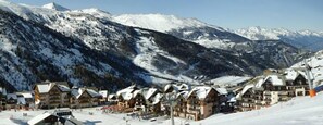 A snow-covered mountain village with traditional wooden buildings, a ski slope, and a clear view of the surrounding mountains. - Hotel L'Aigle (Valmeinier)