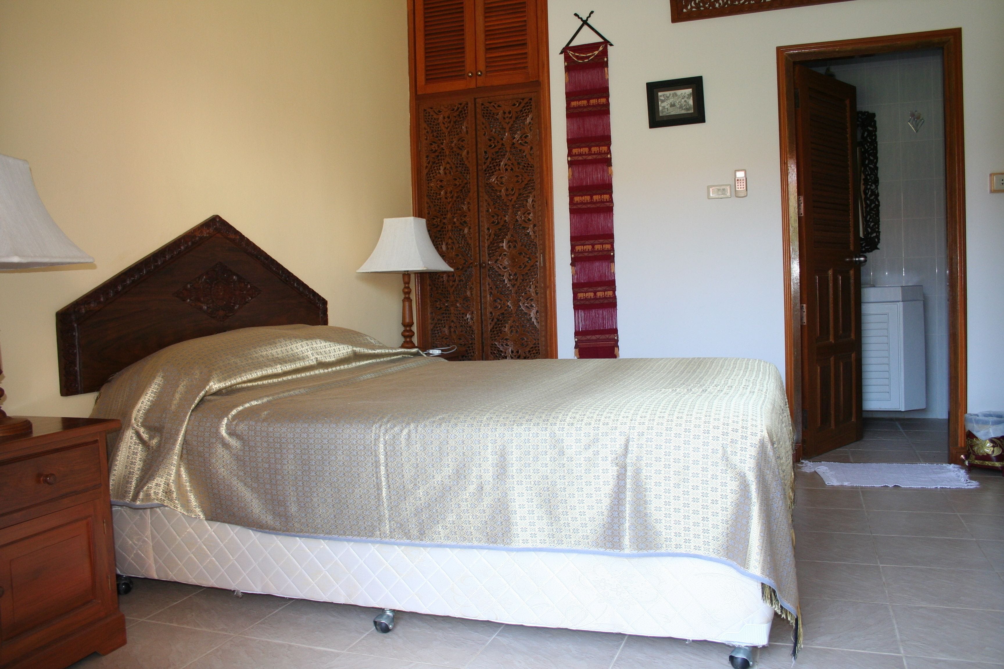 Un dormitorio con cama, cabecero de madera, mesita de noche, lámpara y armario con puerta estampada.