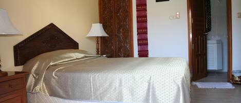 Un dormitorio con cama, cabecero de madera, mesita de noche, lámpara y armario con puerta estampada.