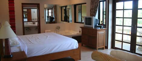 A bedroom with a bed, a TV, a bathroom with a sink and mirror, and a large window.