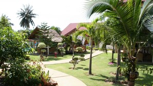 A resort with a well-maintained garden, palm trees, and a thatched-roof building. - Long Beach Inn (Sam Roi Yot)