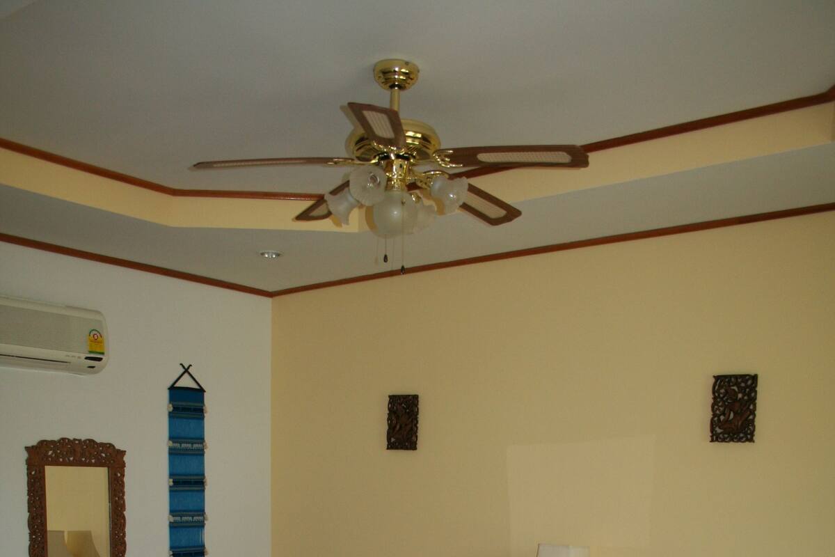 A hotel room with two beds, a ceiling fan, a wooden dresser, and a wall-mounted air conditioner.