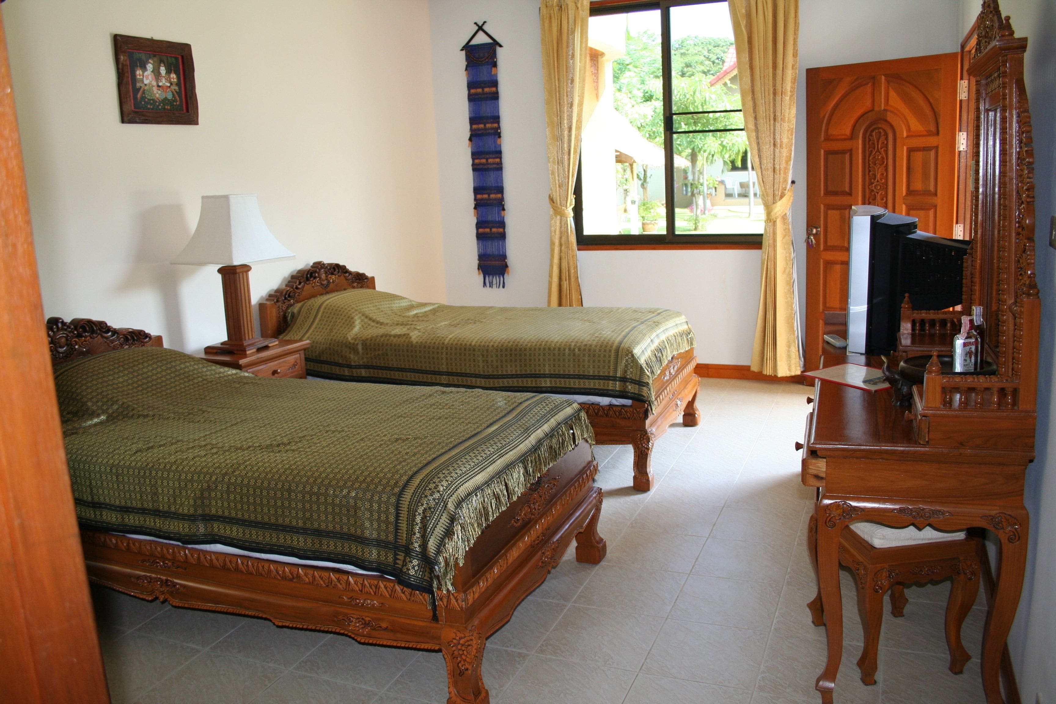 A room with two wooden beds, a wooden dresser, a mirror, and a window with curtains.