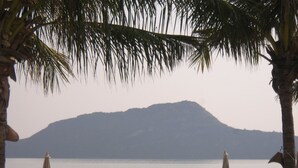 A beachside view with a mountain in the background, palm trees, and beach chairs and umbrellas. - Long Beach Inn (Sam Roi Yot)