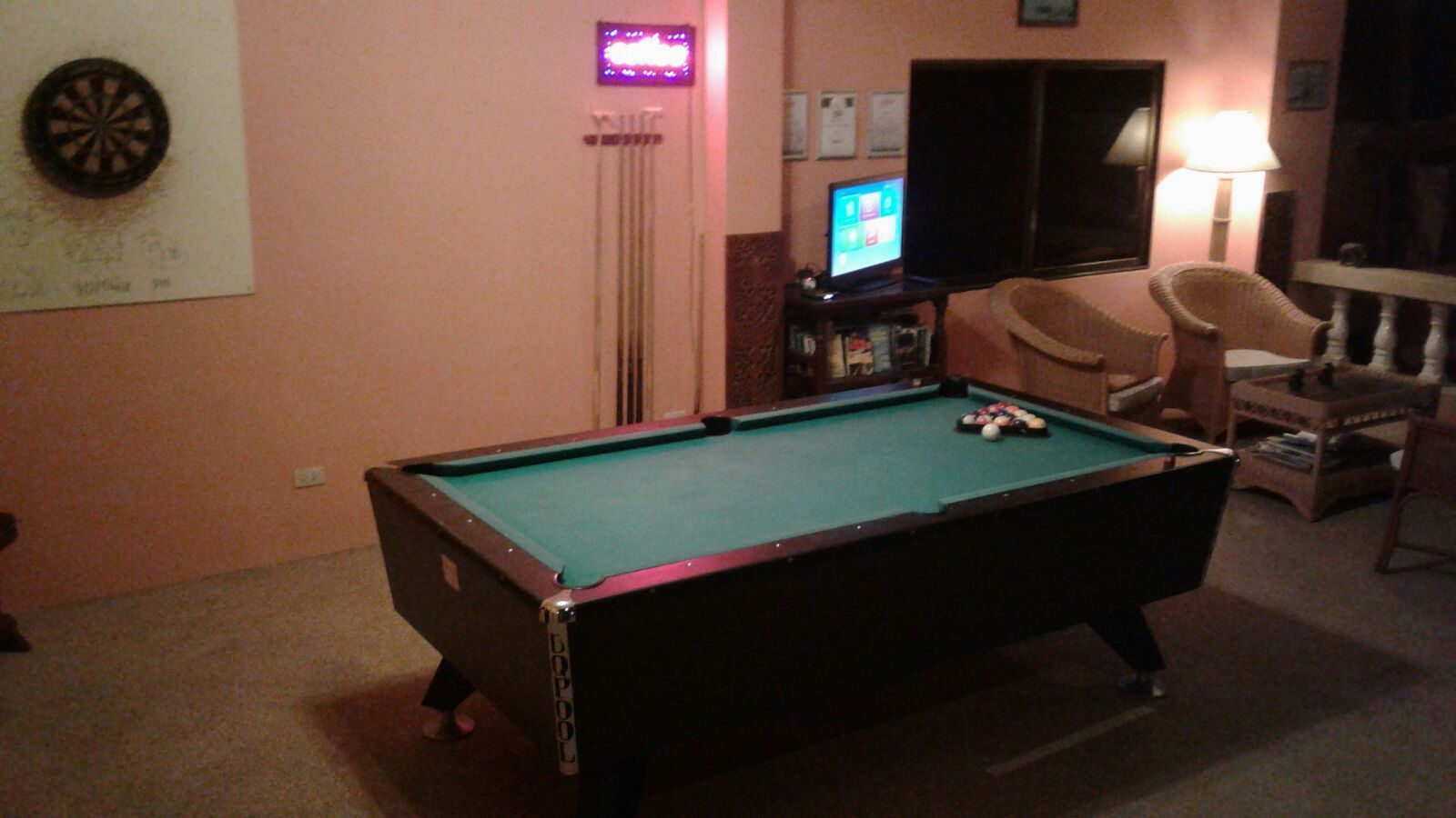 A pool table in a room with a dartboard, a television, and a lamp.
