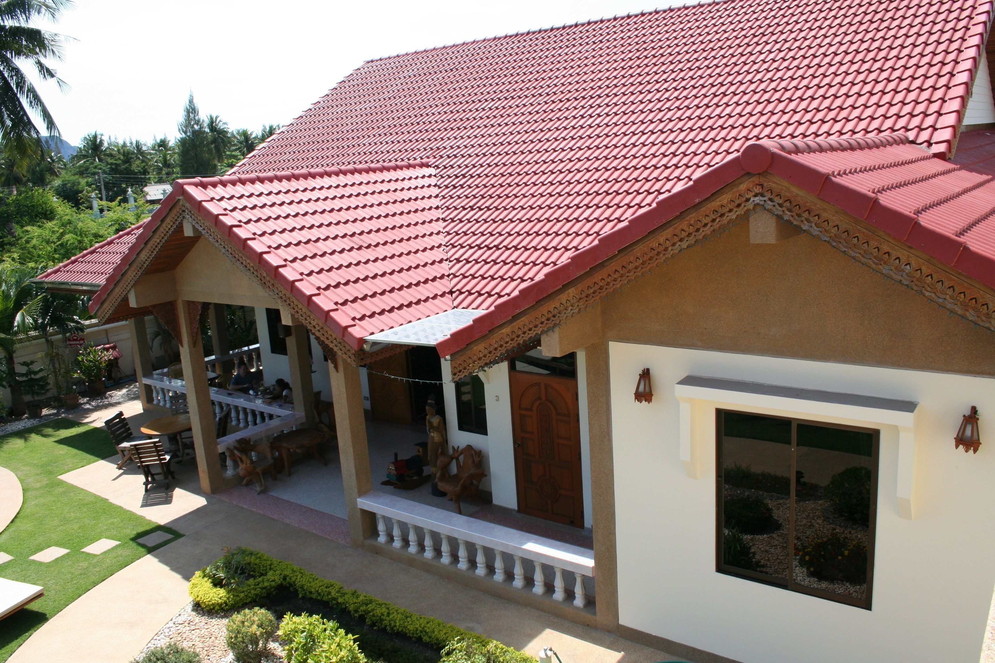 A two-story building with a red-tiled roof, a balcony with seating, and a garden area.