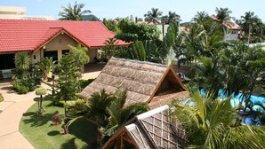 A resort with a red-roofed building, a thatched-roof structure, and a pool surrounded by palm trees. - Long Beach Inn (Sam Roi Yot)