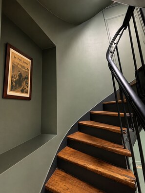 A staircase with wooden steps and a metal railing, leading to a landing with a framed picture on the wall. - Hotel de France (Paris)