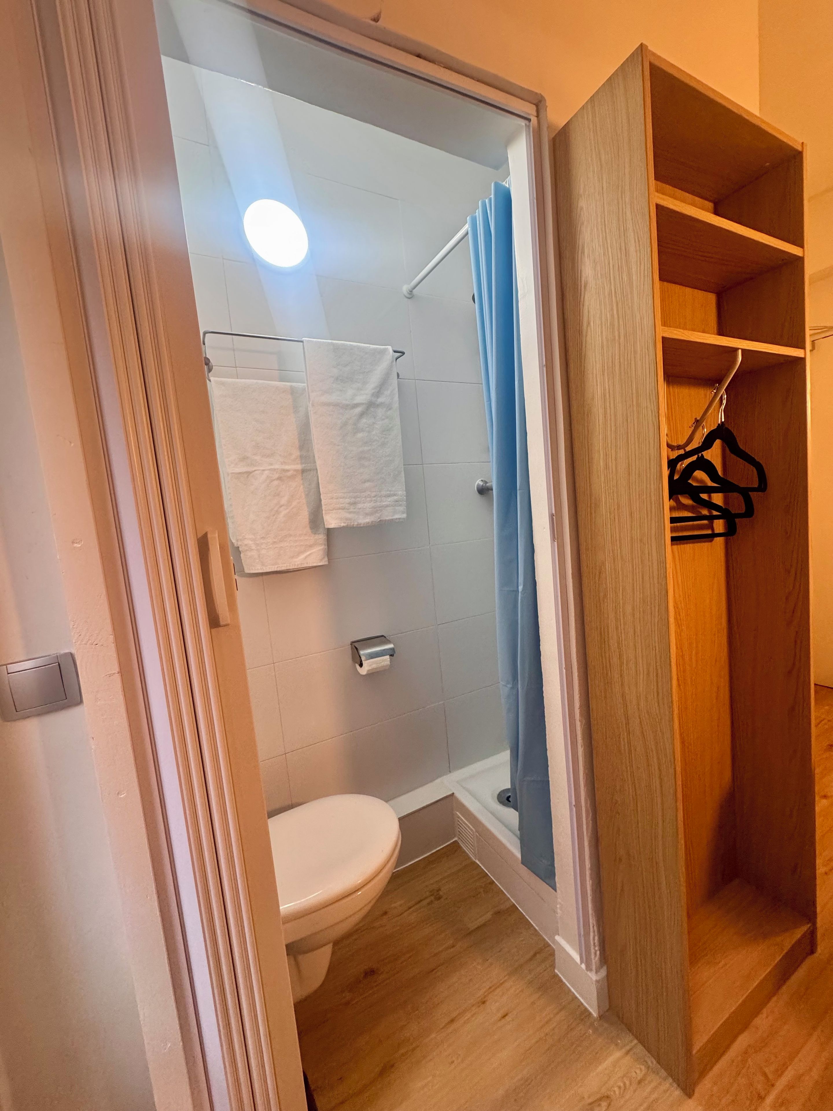 Ein Badezimmer mit Toilette, einer Duschkabine mit Glastür und einem Holzschrank mit Kleiderhaken.