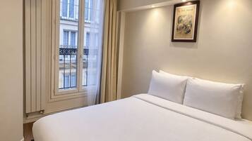 Habitació d'hotel amb un llit gran, una televisió penjada a la paret, una finestra amb cortines i un quadre amb marc a la paret.