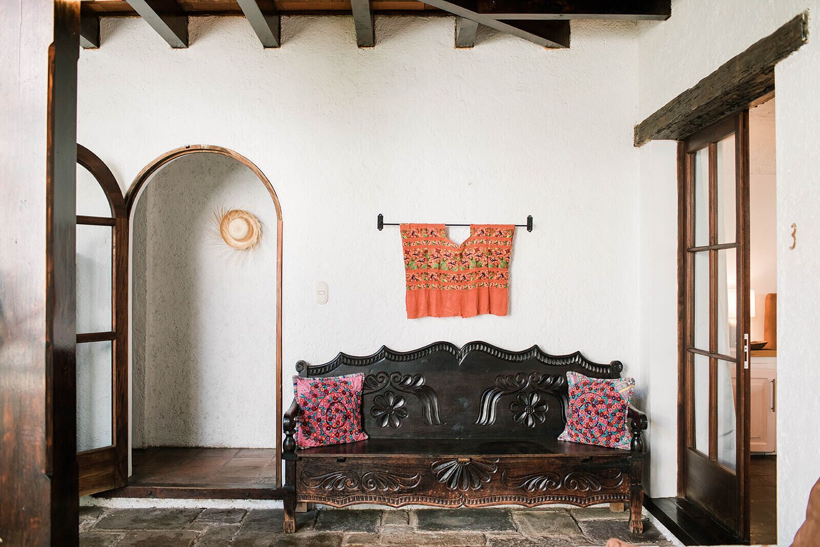 A wooden bench with ornate carvings, a patterned cushion, and a hanging garment.