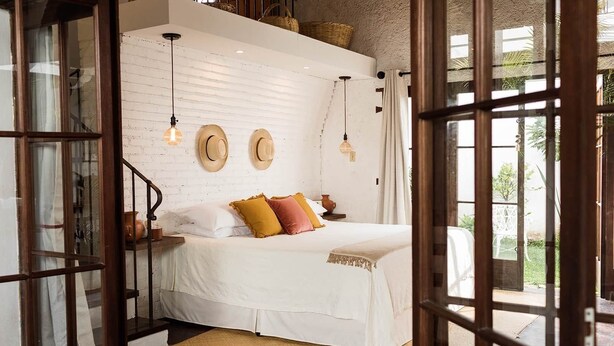 Un dormitorio con cama blanca, cabecera de madera y tres sombreros colgados en la pared.
