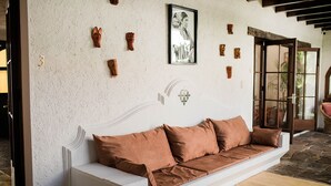 Un sofá blanco con cojines marrones en una habitación con pared blanca texturizada, una fotografía blanco y negro enmarcada, y varias tallas de madera.