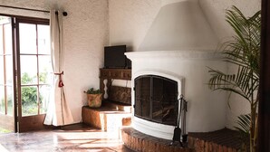 Una habitación acogedora con chimenea, una ventana con cortinas, un banco de madera y una planta en maceta.