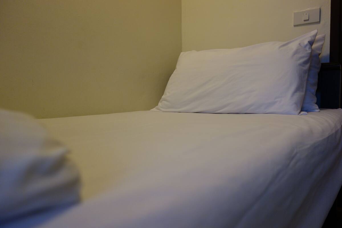 Un lit simple avec une literie blanche, dans une pièce aux murs de couleur unie.