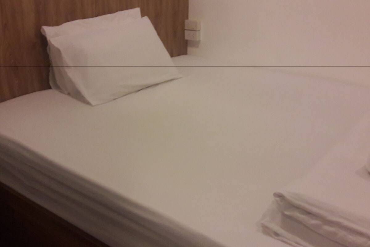 Un lit bien fait, avec du linge de lit blanc, une tête de lit en bois et un mur blanc.