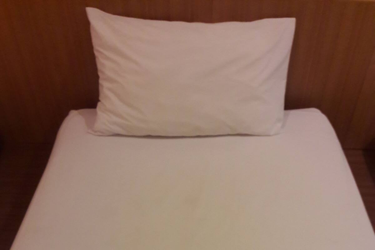 Un lit simple avec un matelas blanc et un oreiller blanc, dans une pièce aux murs en bois.