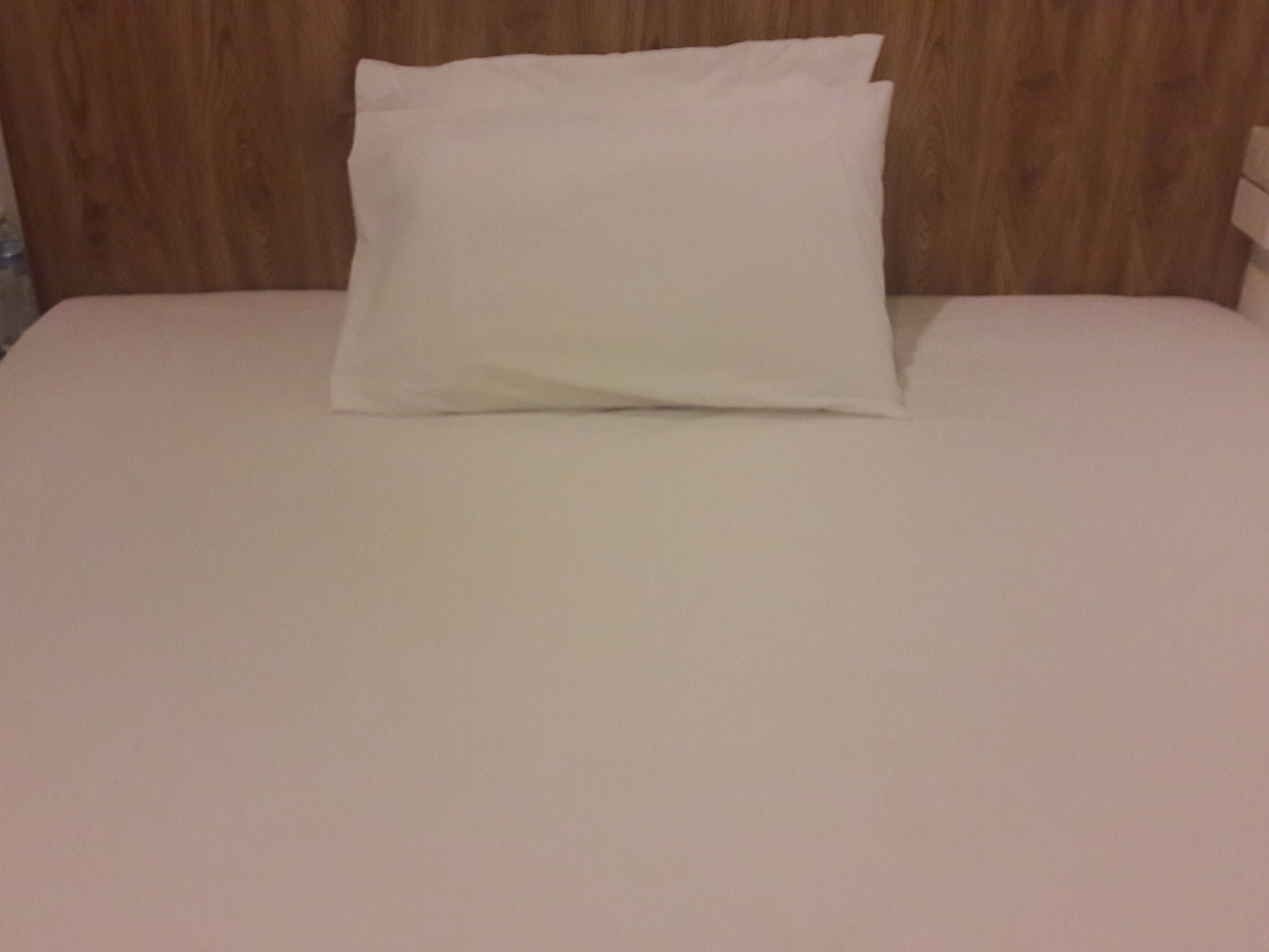 A neatly made bed with a white pillow and a white bedsheet.