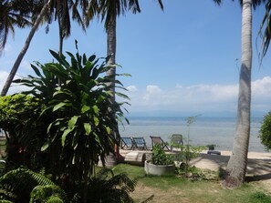 A tropical outdoor seating area with palm trees, a concrete planter with plants, and a view of the sea. - Bird Bungalow (Ko Pha-ngan)