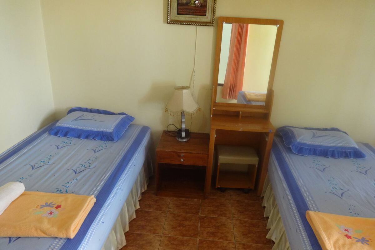 Una habitación pequeña y sencilla con dos camas individuales, una mesita de noche, un espejo y una lámpara.