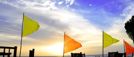 A beach with wooden chairs and tables, flags, and a view of the ocean.
