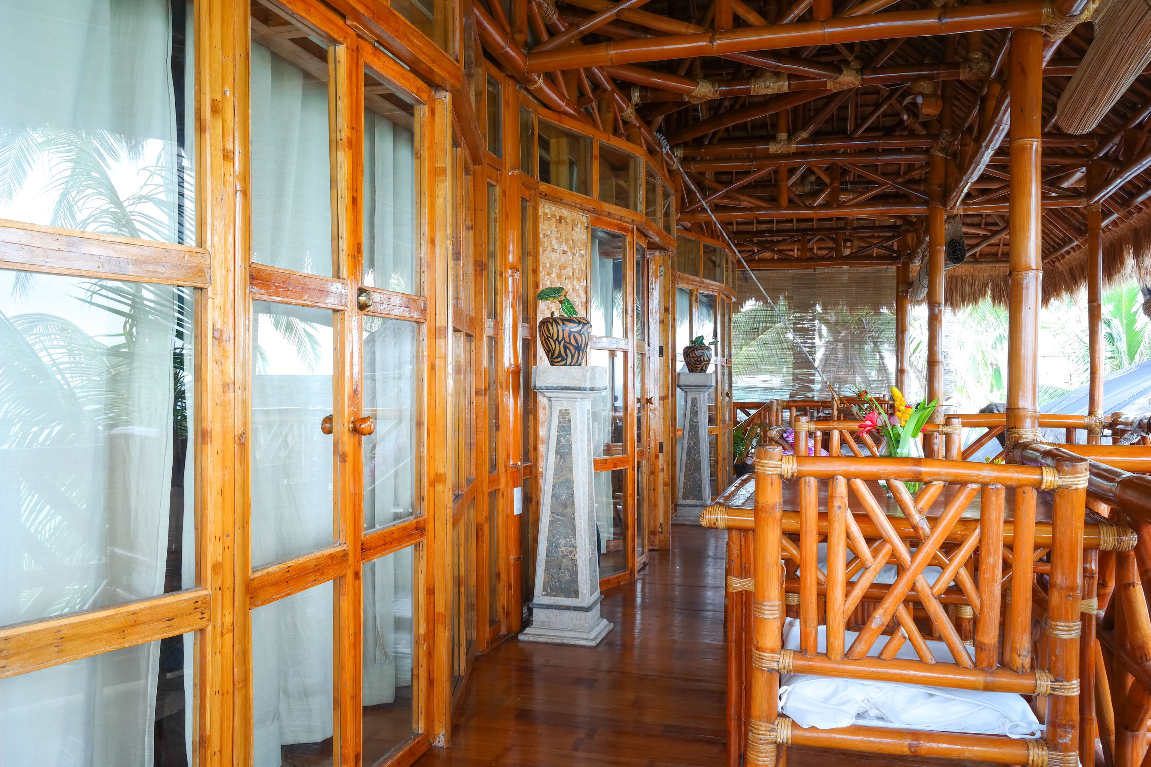 A covered walkway with wooden railings and a polished floor, leading to a seating area with cushions.