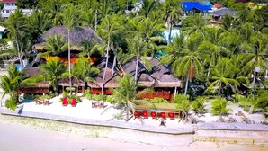 A beachfront property with thatched-roof structures, palm trees, and a sandy beach. - The Coral Blue Oriental Beach Villas & Suites (Santa Fe)