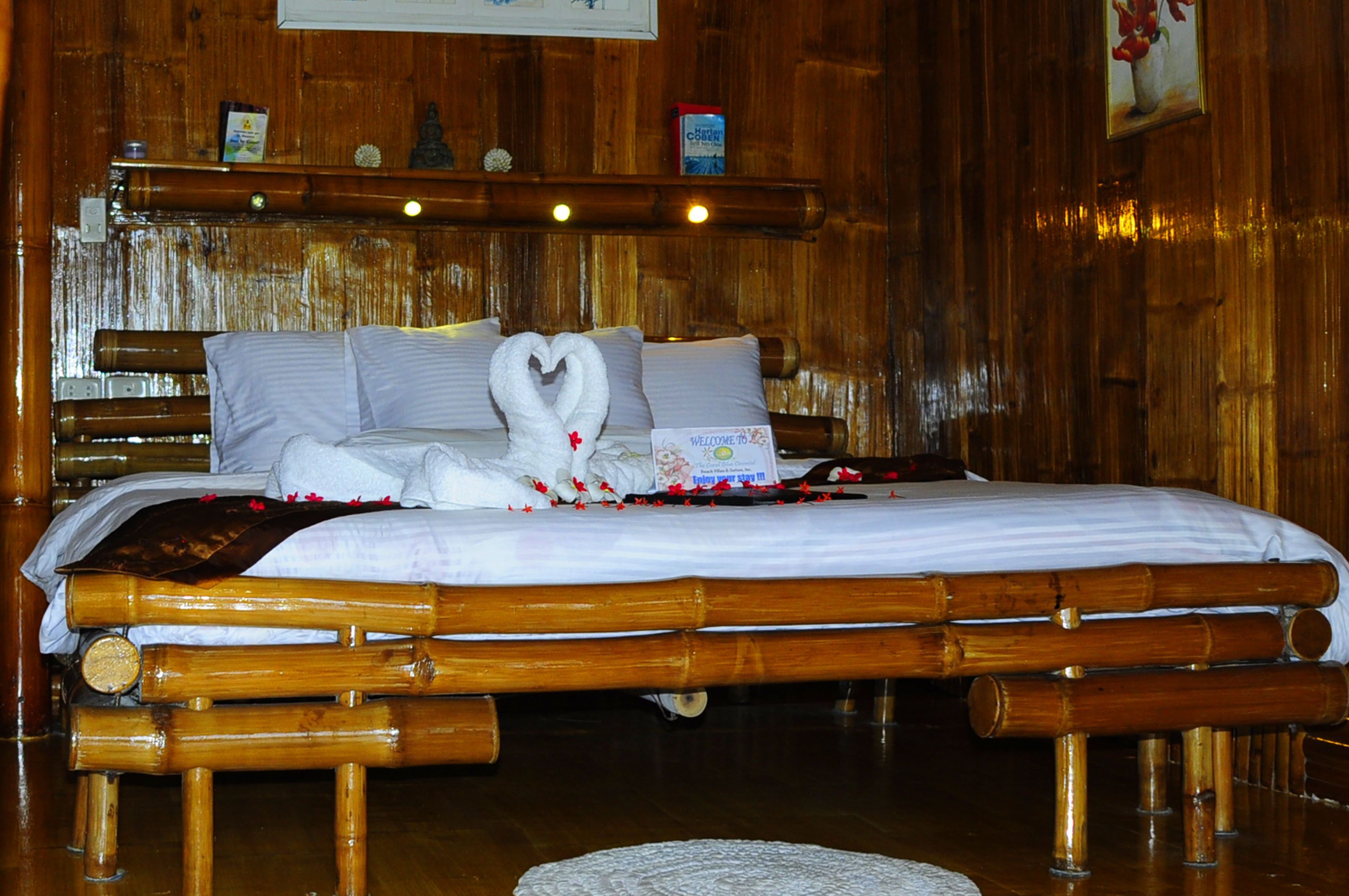 A bed with a heart-shaped towel arrangement, a welcome sign, and a framed picture on the wall.