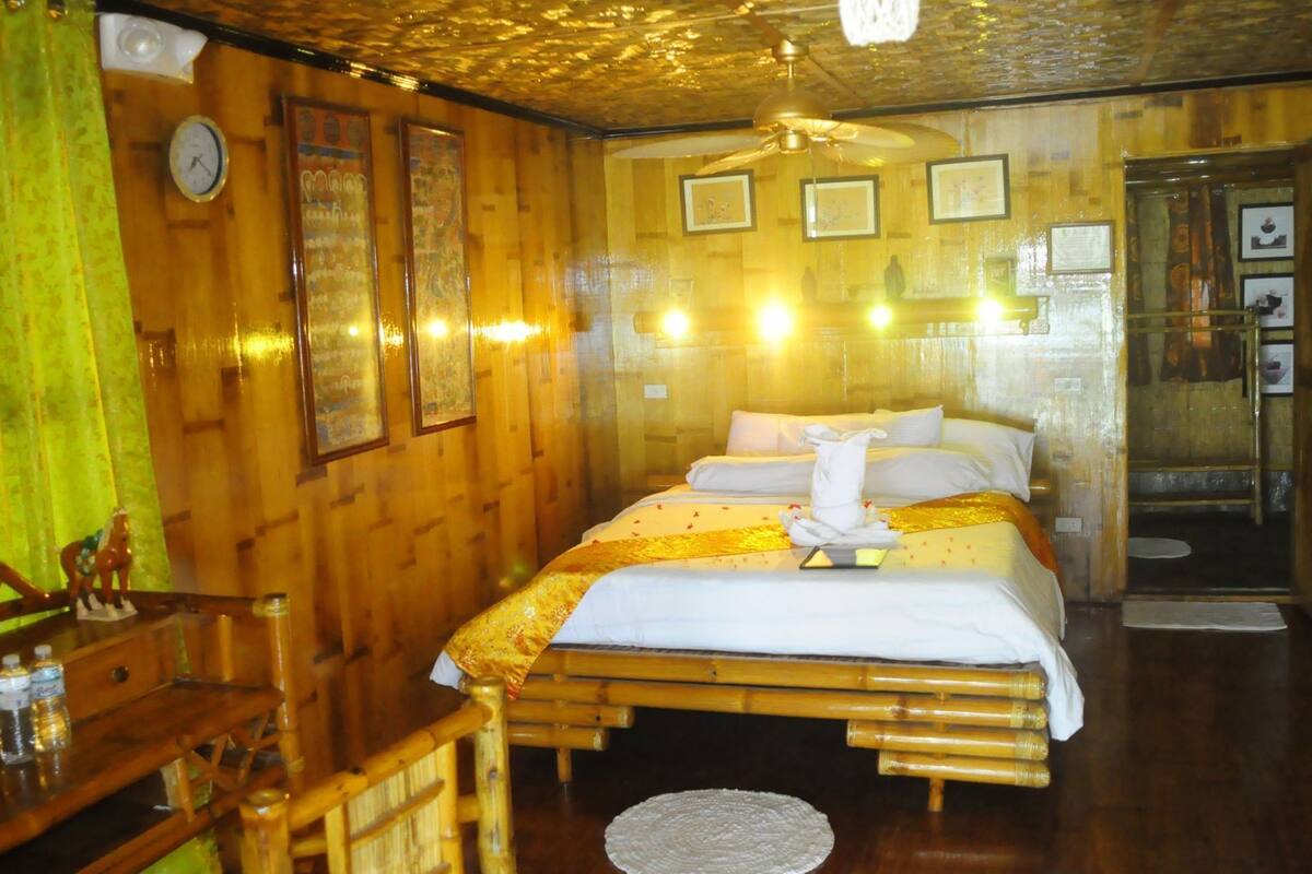 A wooden room with a bed, a clock, framed pictures, and a wooden bench.