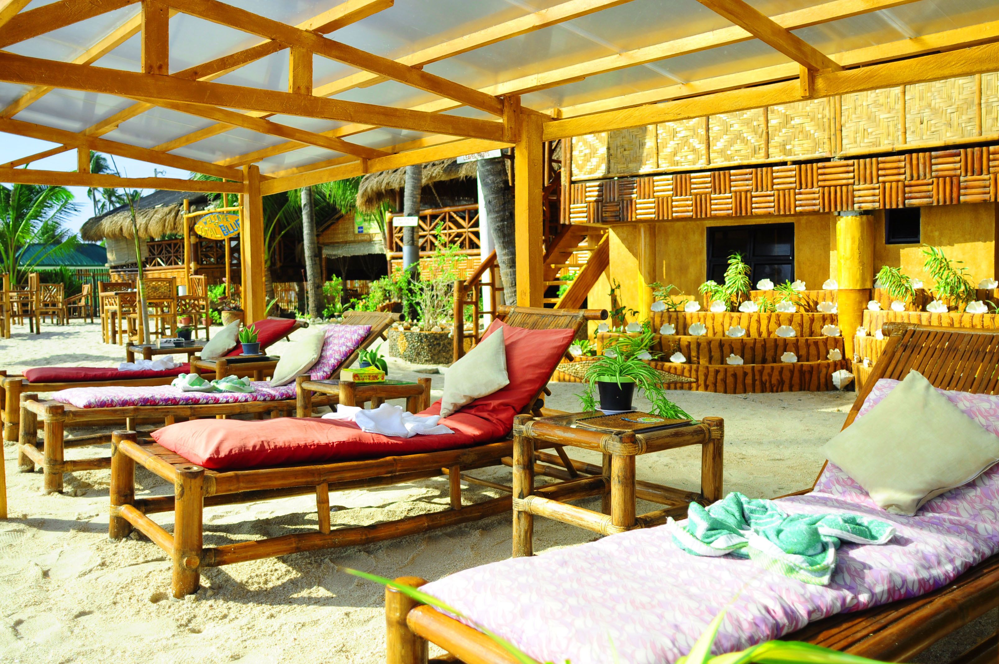 A beachside lounge area with wooden loungers, a thatched-roof structure, and tropical plants.