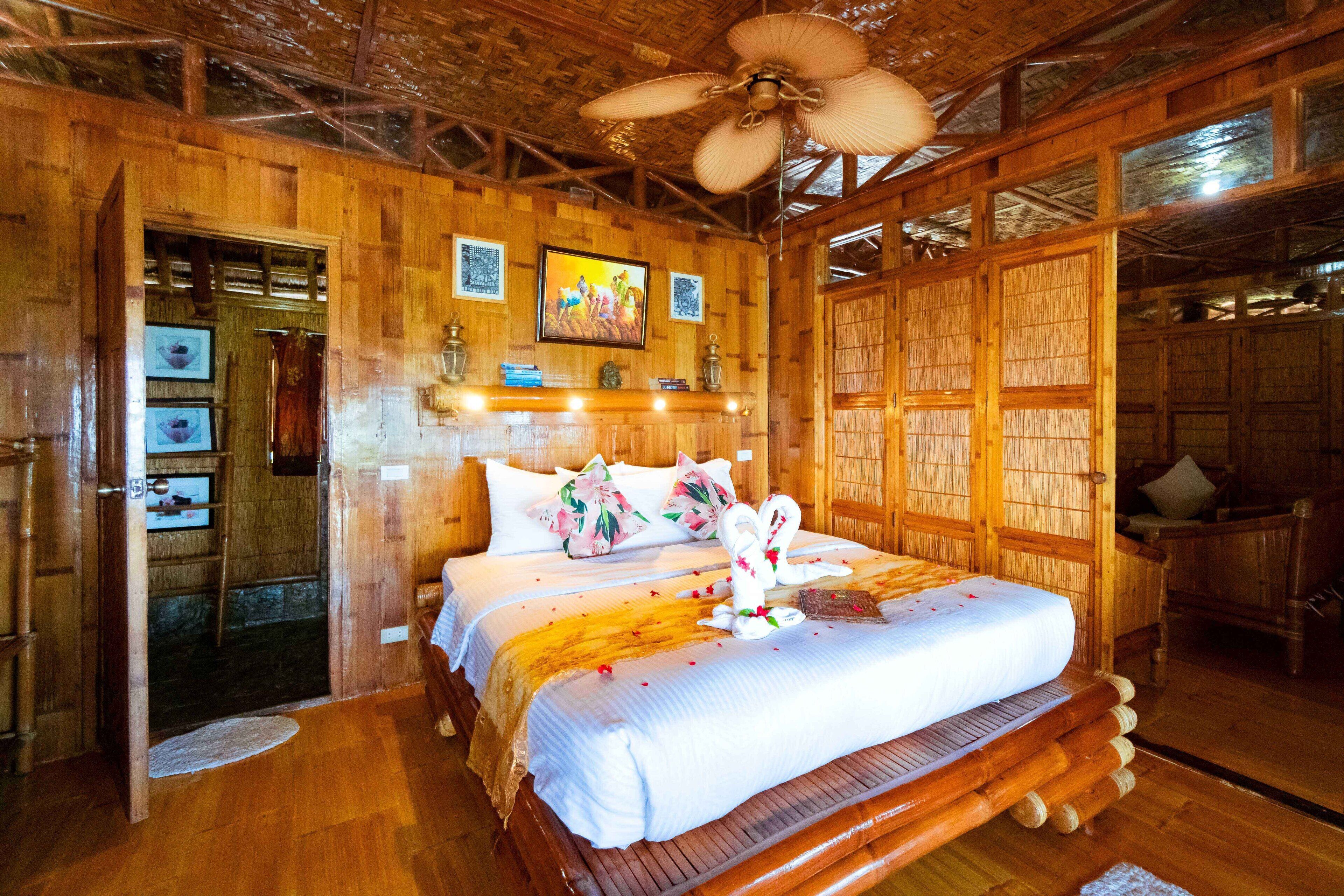 A wooden room with a bed, a ceiling fan, and wooden walls.