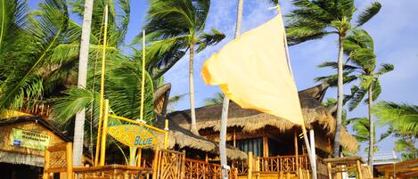 Un restaurante frente a la playa con techos de paja y mobiliario de bambú.