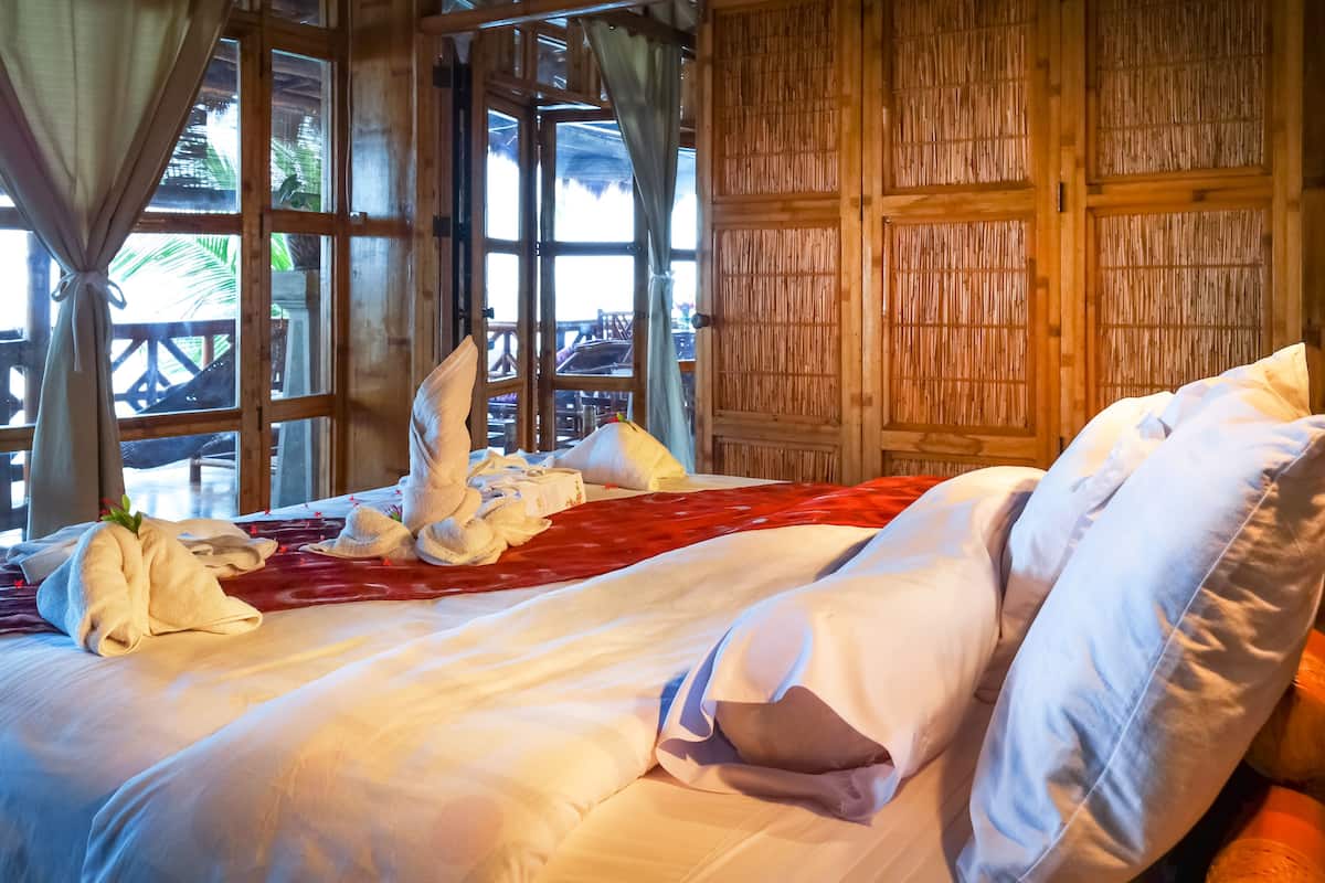 A hotel room with a bed, wooden walls, and large windows.