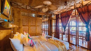 A wooden room with a bed, a ceiling fan, and large windows with curtains. - The Coral Blue Oriental Beach Villas & Suites (Santa Fe)