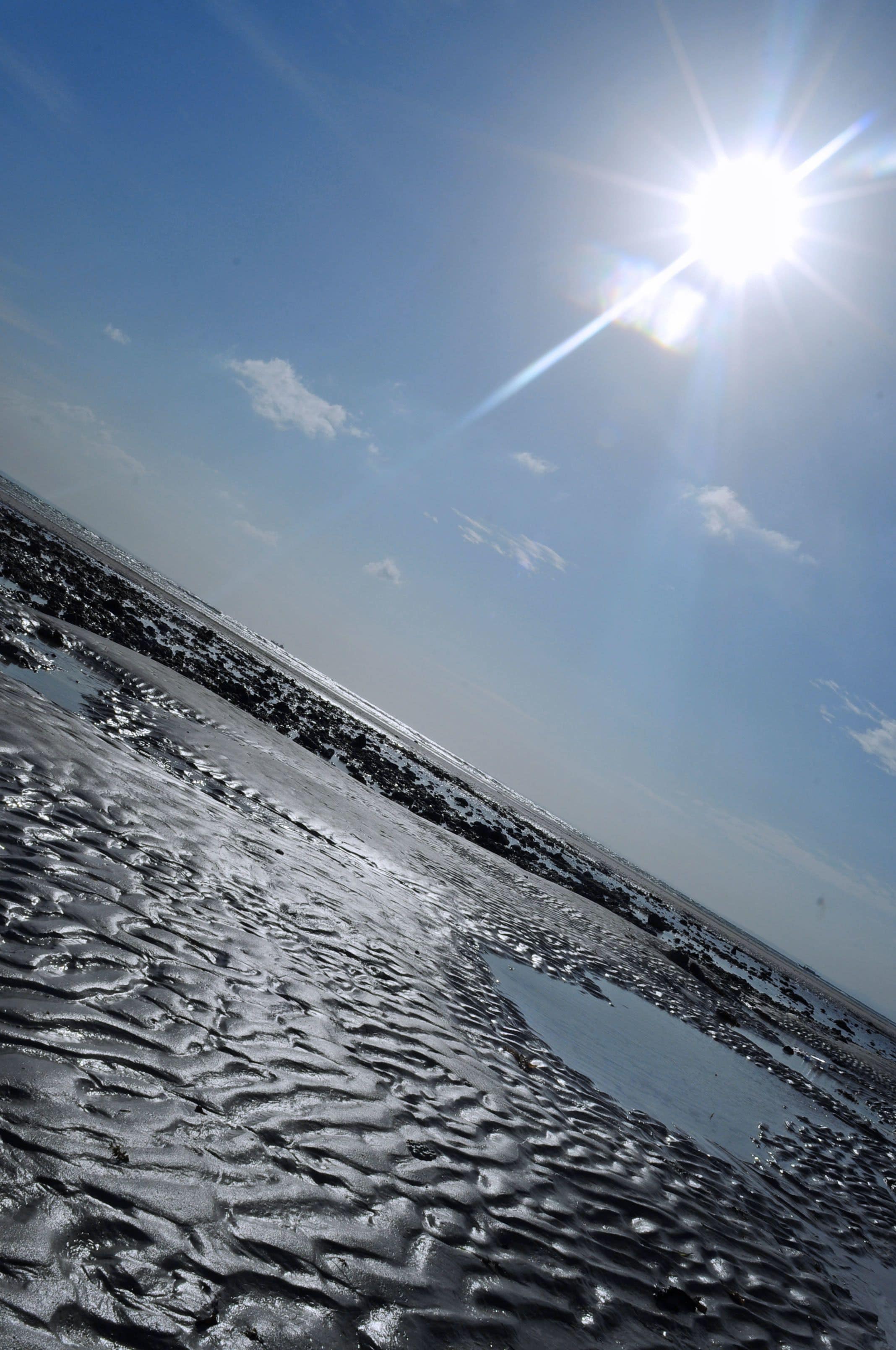 Een strand met nat zand en een heldere lucht.
