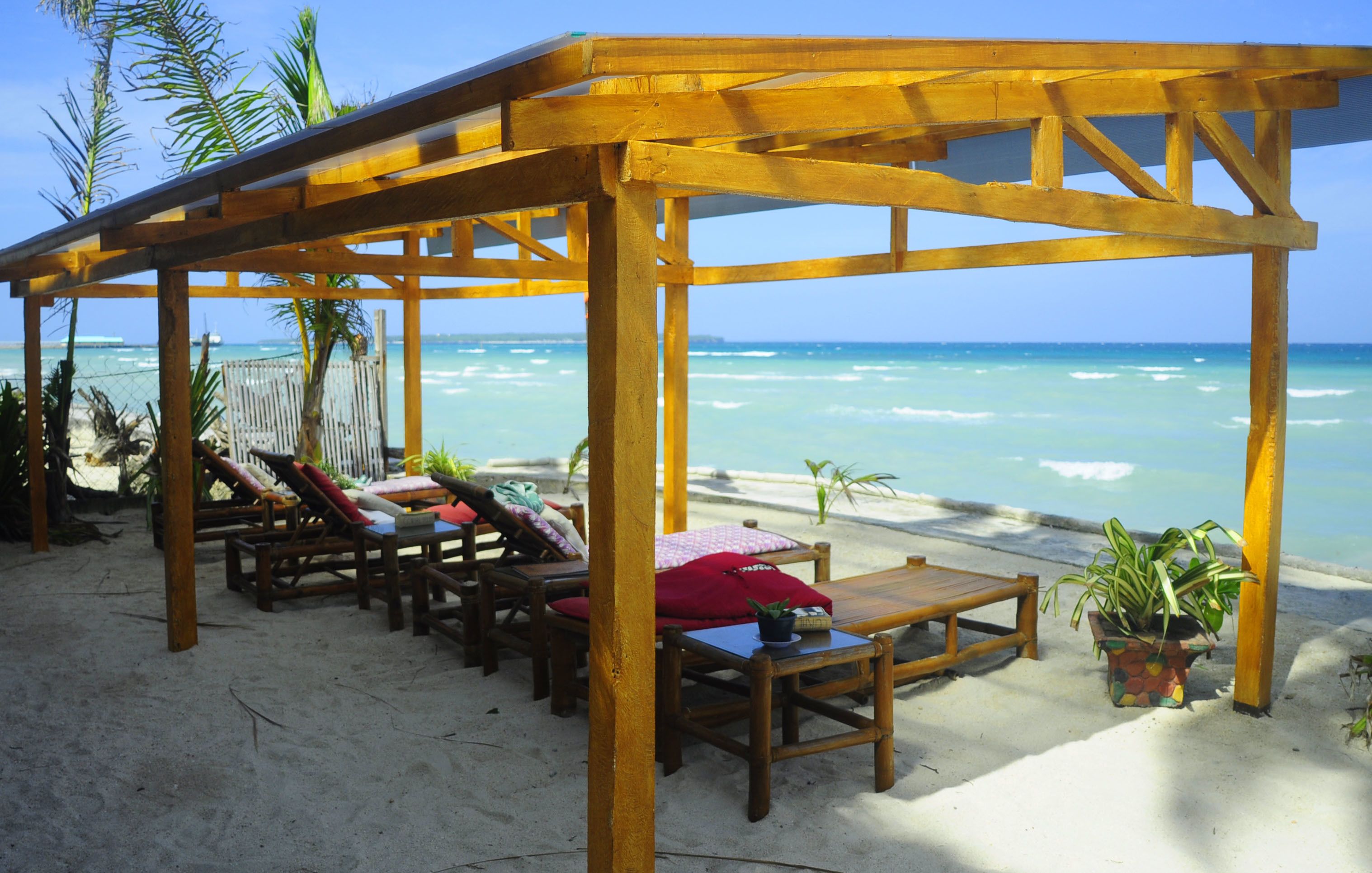 A wooden beach cabana with lounge chairs and a table, overlooking the ocean.