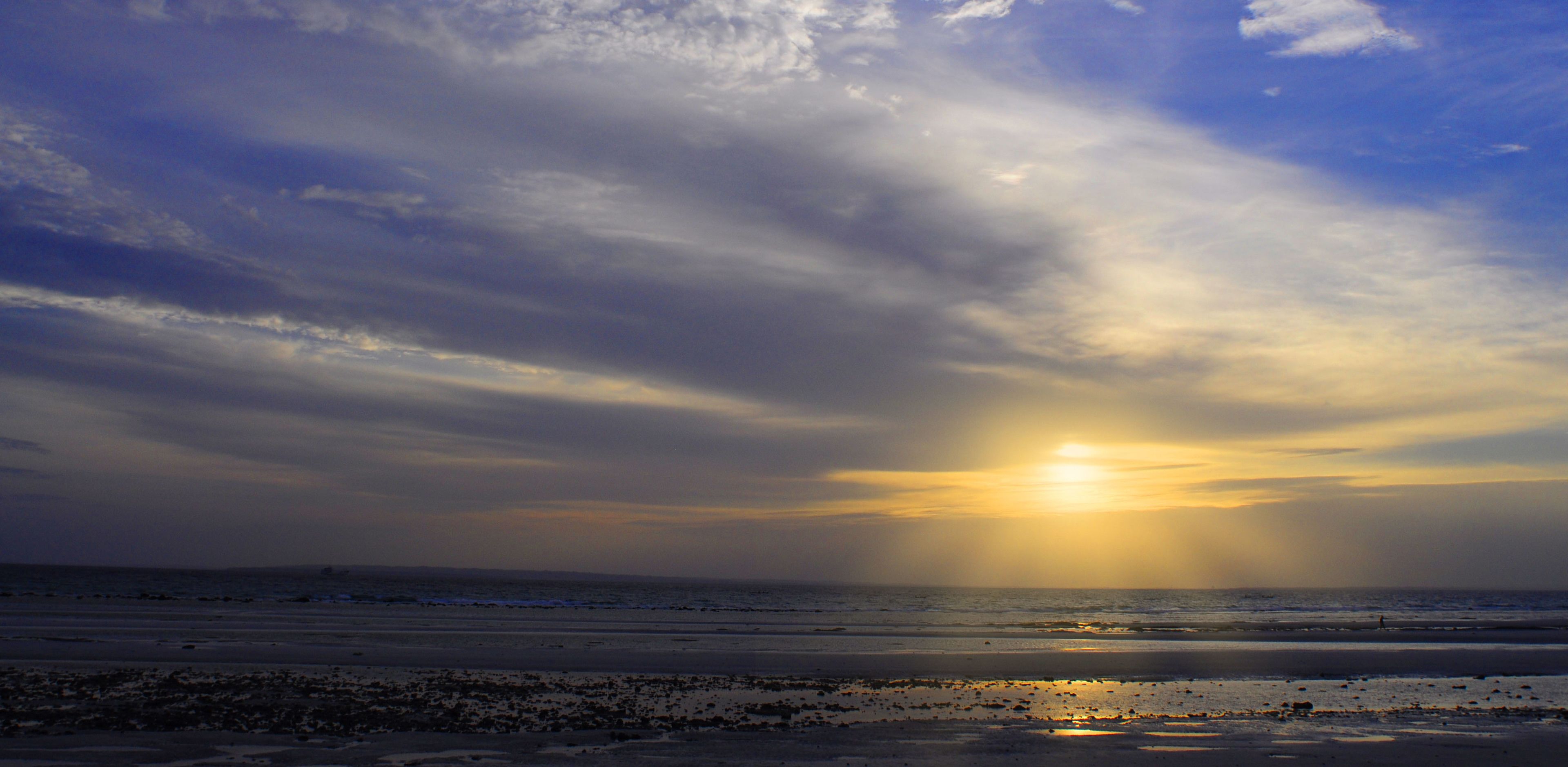 Une plage au coucher du soleil, avec des nuages et l’océan.