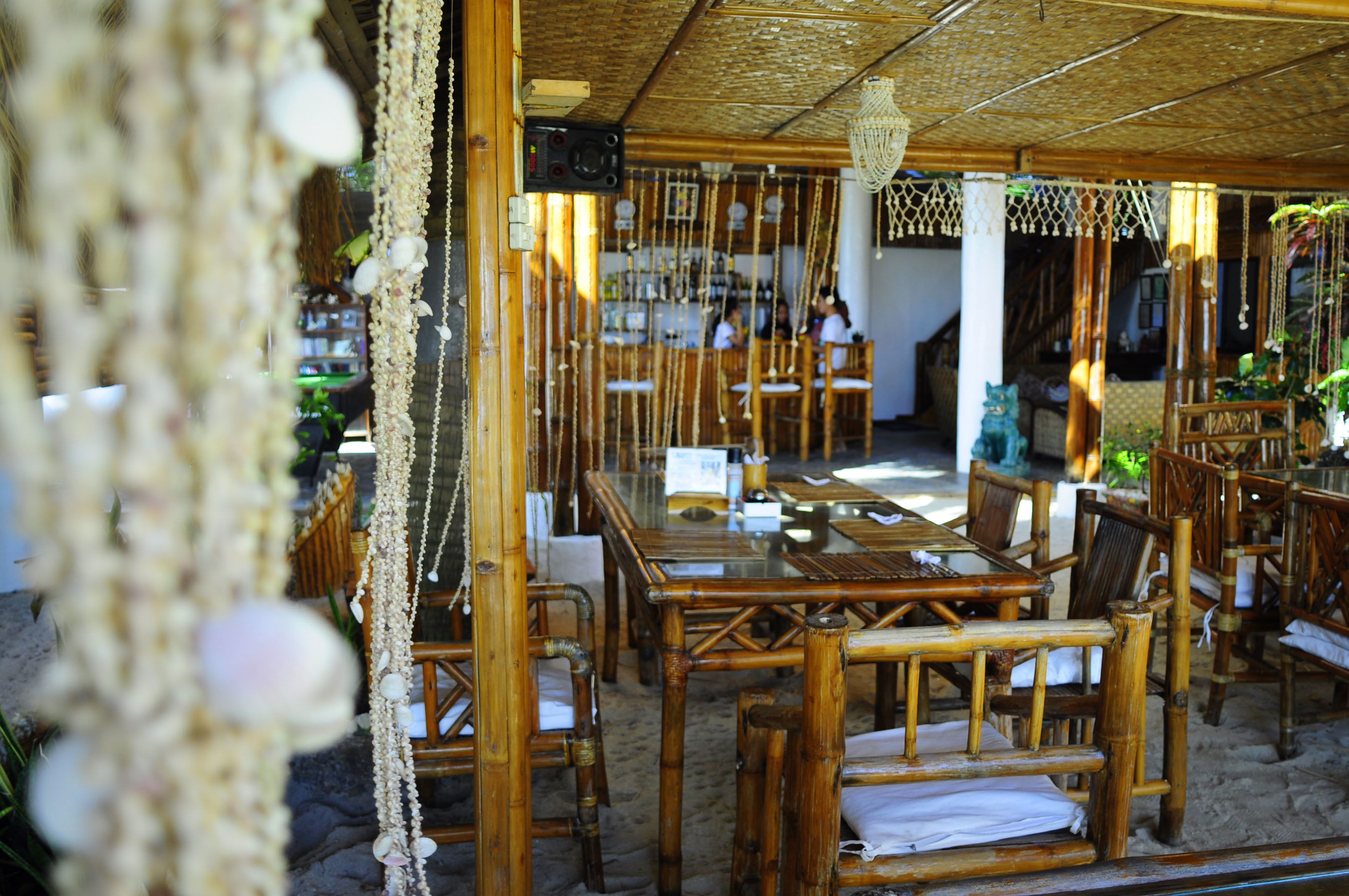 An outdoor restaurant with bamboo furniture and a thatched roof.