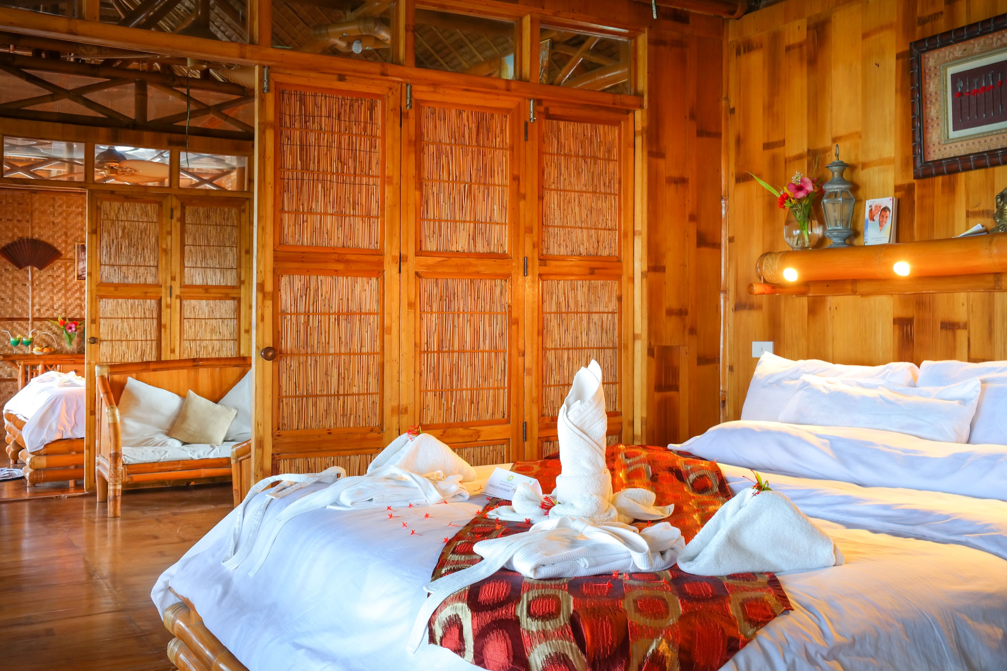 A wooden room with a bed, a chair, and a wall with a fan.