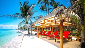 A beachside resort with a covered seating area, palm trees, and a clear view of the ocean. - The Coral Blue Oriental Beach Villas & Suites (Santa Fe)