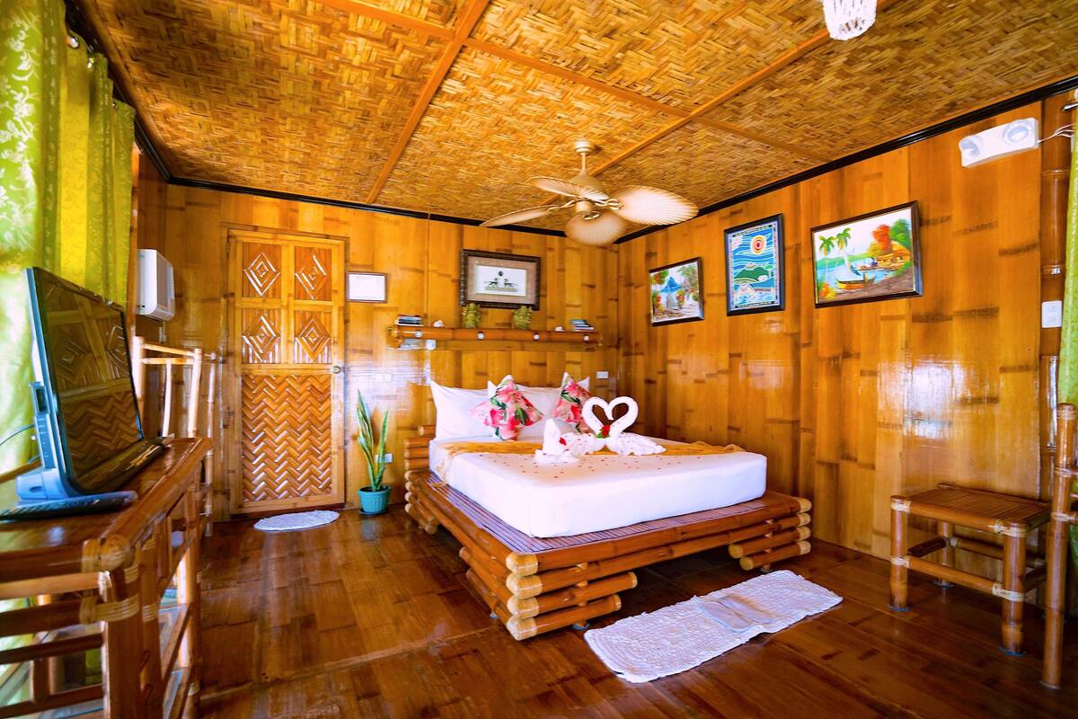 A wooden-themed room with a bed, a ceiling fan, and framed pictures on the walls.