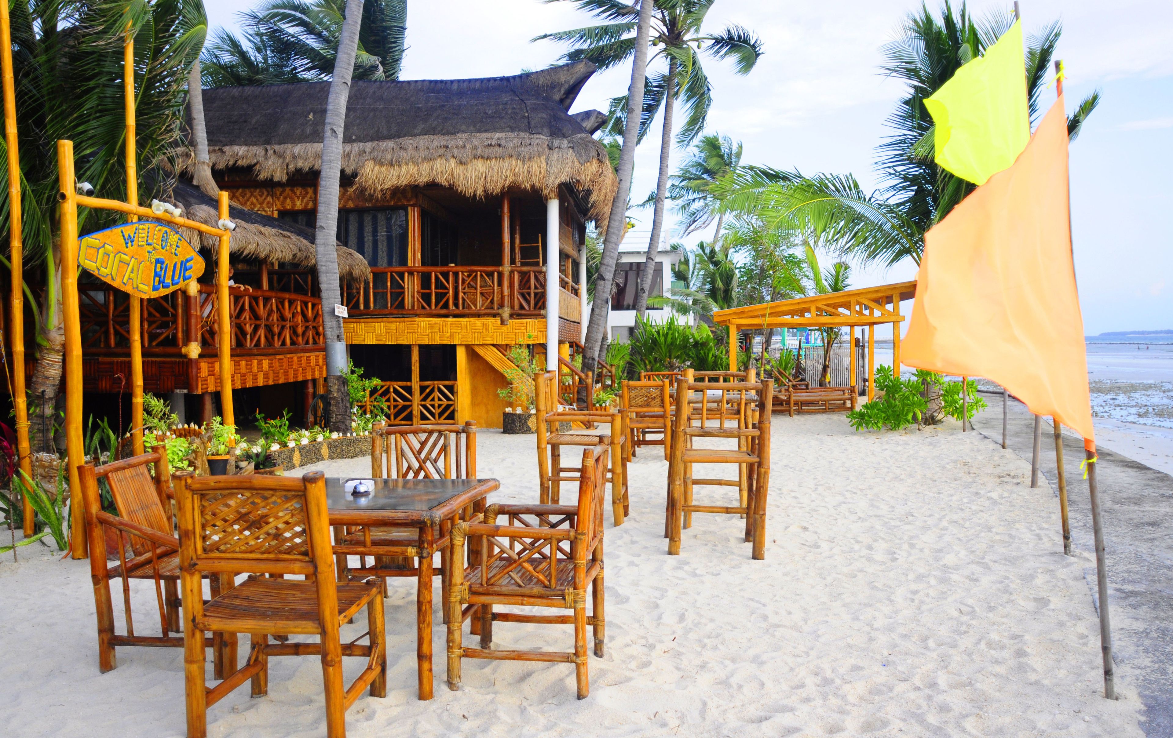 A beachside restaurant with bamboo furniture and a thatched-roof building.