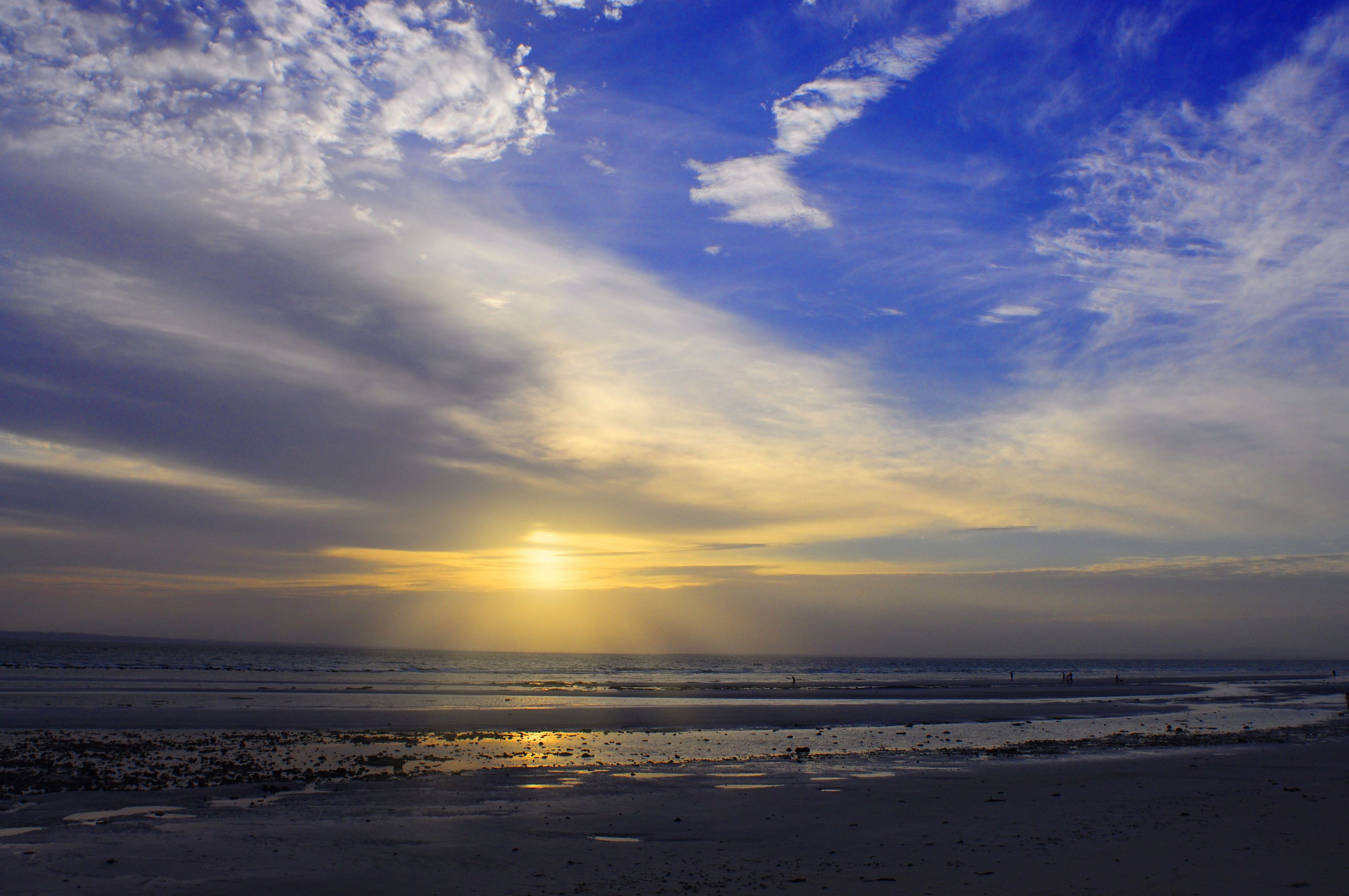 A beach with the sun setting over the horizon, creating a silhouette of the landscape.