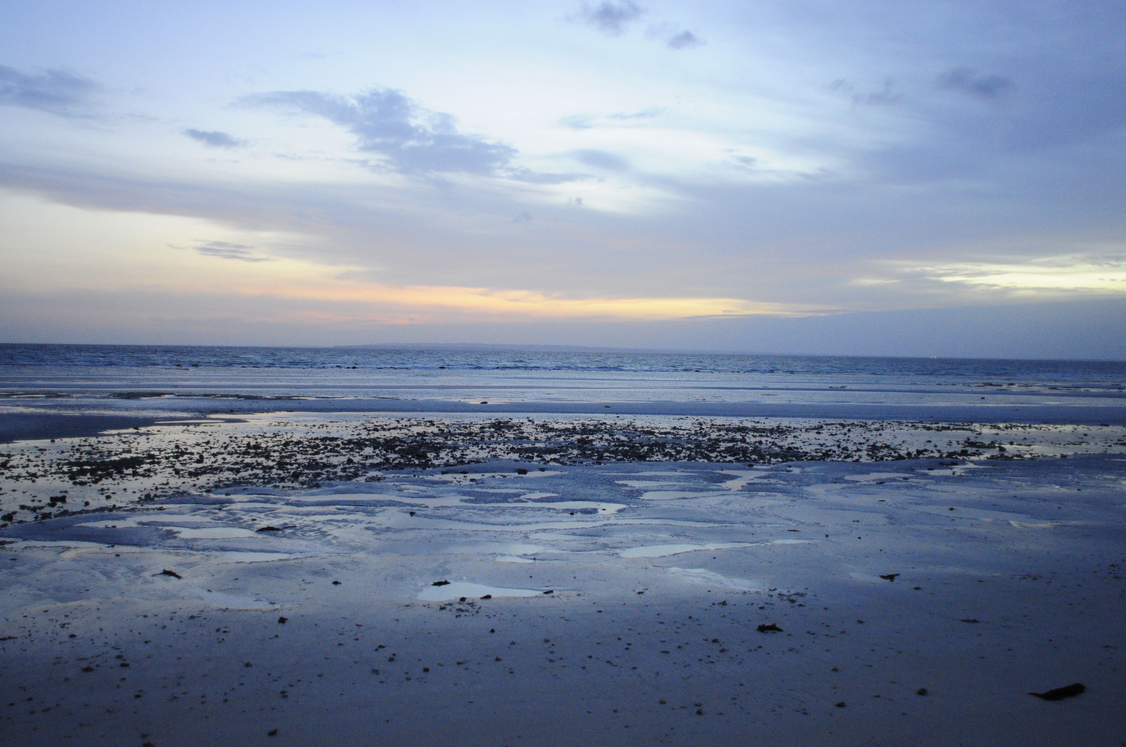 A beach with a wide expanse of sand and a calm sea under a cloudy sky.